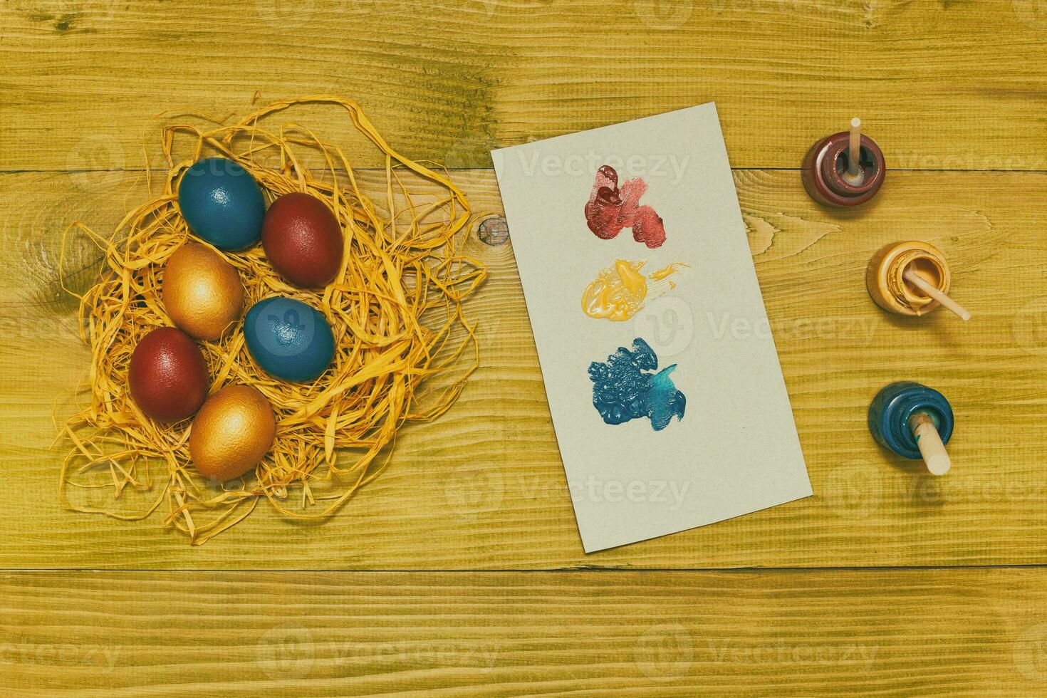 Painted Easter eggs in straw and colors for painting on wooden table.Toned photo. photo