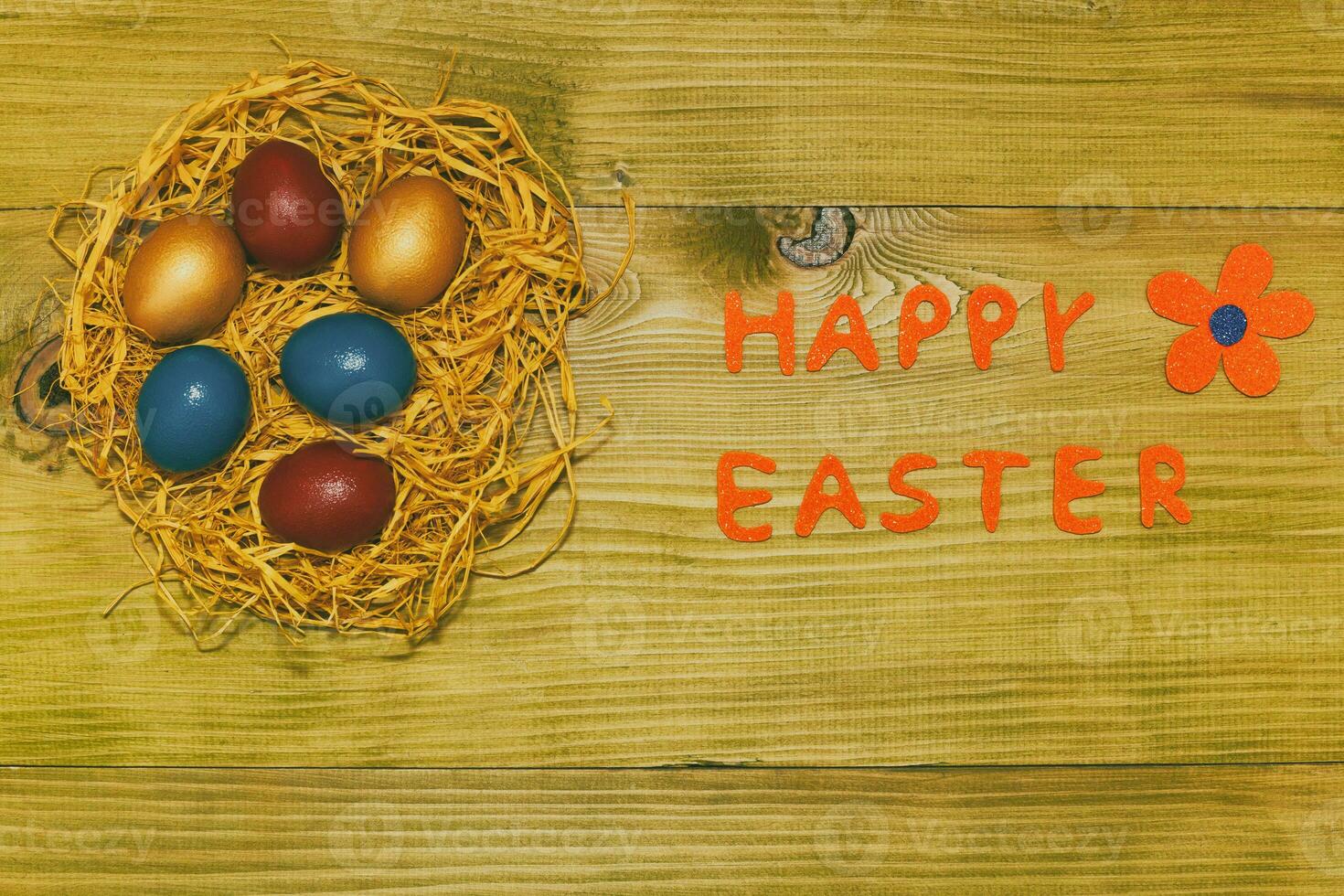 Happy Easter message with painted eggs in straw and flower on wooden table.Toned photo. photo