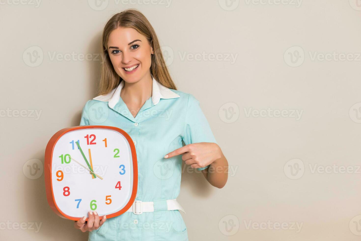 Portrait of medical nurse pointing at clock. photo