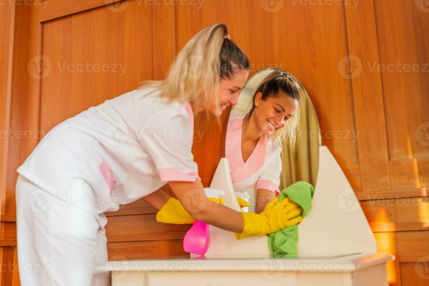 Beautiful hotel maid cleaning mirror in a room. Focus on a mirror. photo