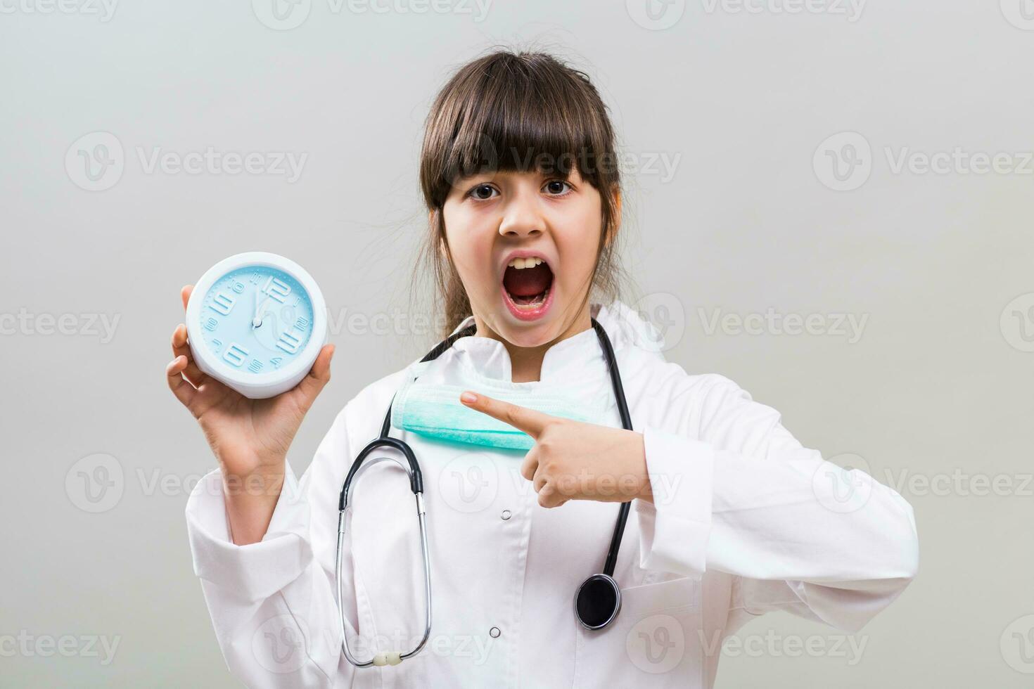 Little doctor is showing that is time to think about health by pointing at clock. photo