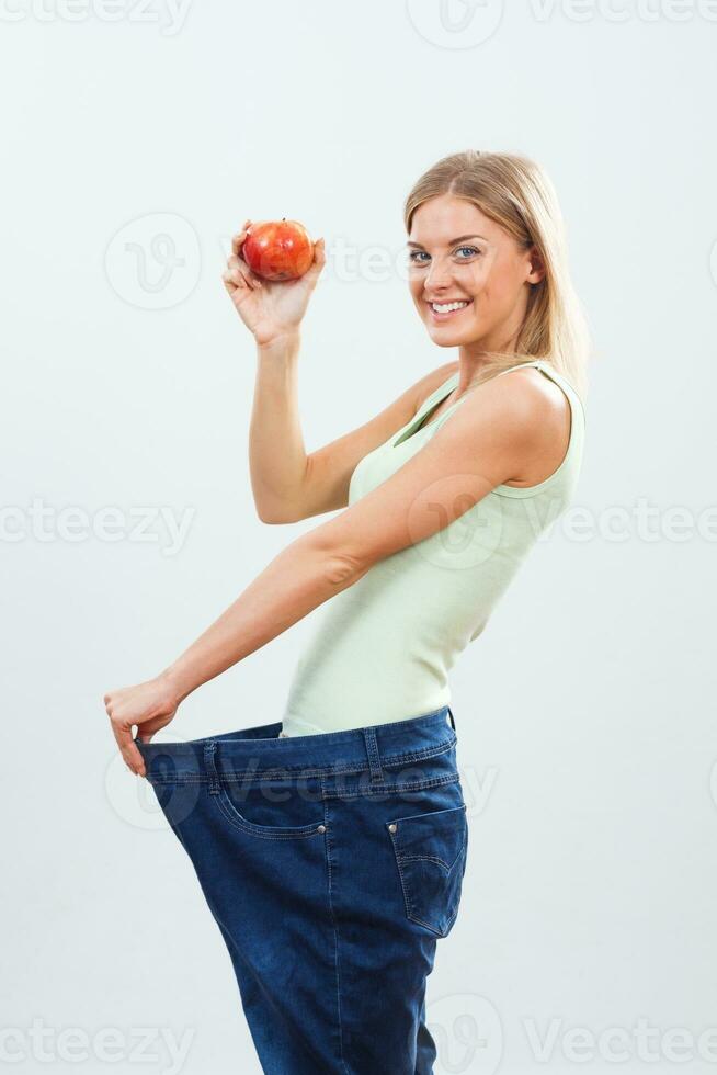 Happy woman in large jeans holding apple.Weigt loss concept. photo