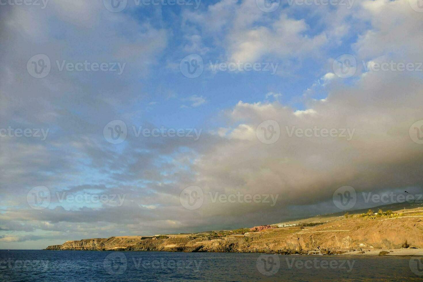 a view of the ocean and a hill with clouds photo