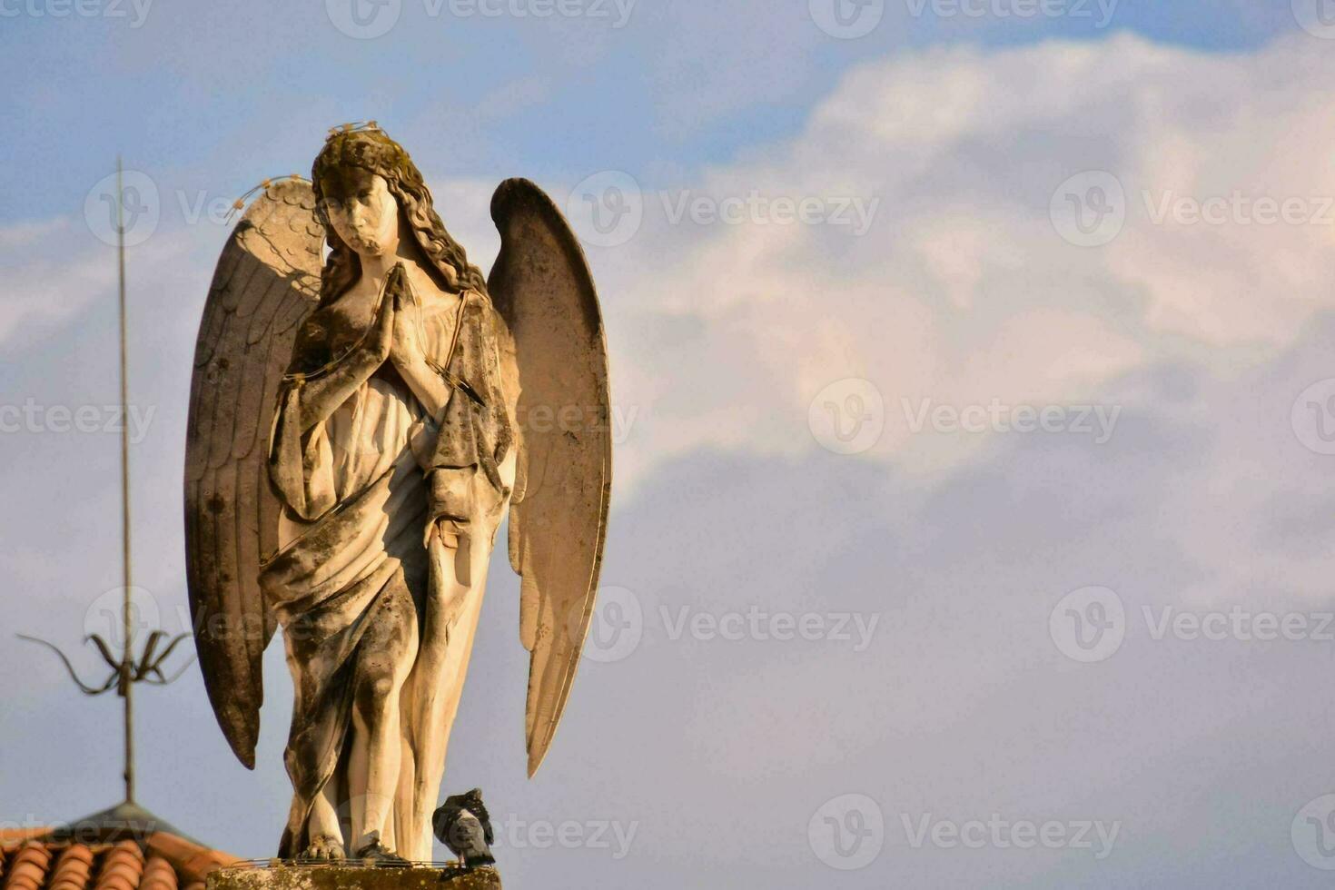 an angel statue on top of a roof with clouds in the background photo
