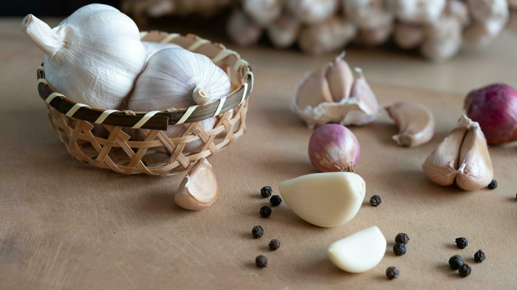 orgánico crudo ajo bulbo en bambú cesta en un de madera mesa y ajo clavos de olor, cebollas, negro granos de pimienta de comida ingredientes foto