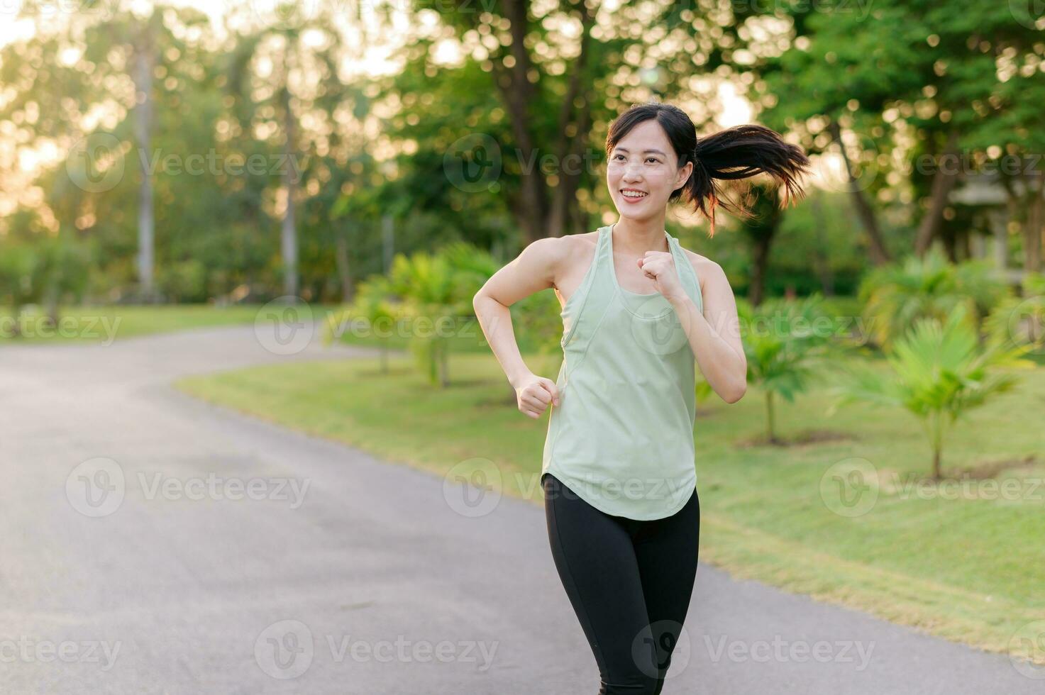 Fit Asian young woman jogging in park smiling happy running and enjoying a healthy outdoor lifestyle. Female jogger. Fitness runner girl in public park. healthy lifestyle and wellness being concept photo