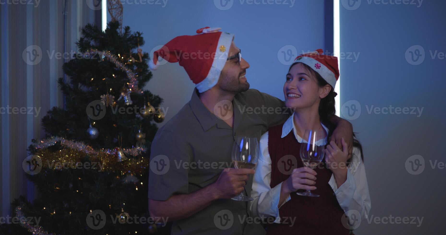 Portrait of  Young man are embracing their girlfriends, holding a glass of wine and enjoying standing beside the Christmas tree in the room,Lovers have moment romantic and happy together photo