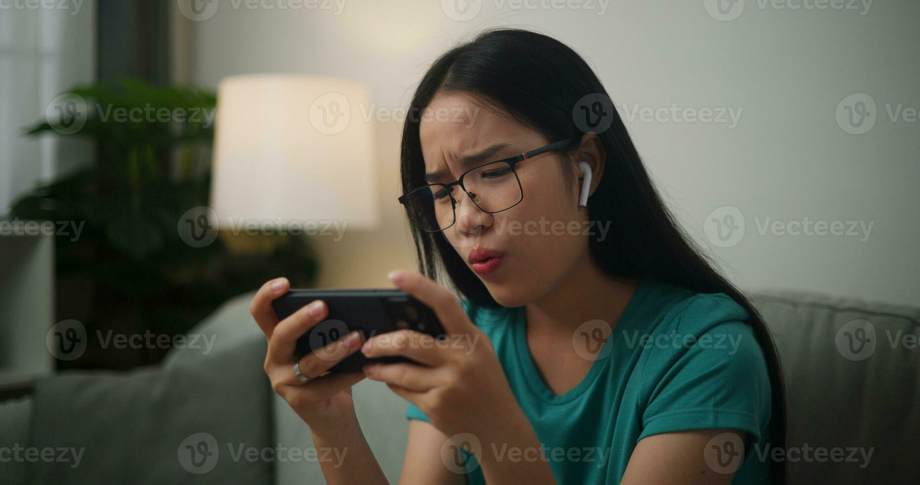 Portrait of Young Asian woman serious playing an online game frustrated with loss or failure sitting on sofa in living room at home.Gamer lifestyle concept. photo