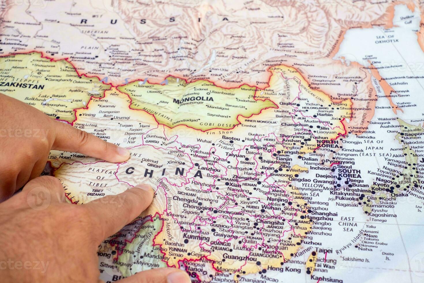 Tourist's hand pointing at world map of China. Located in Asia on world map, China is a country with a large area and a large population. top view photo