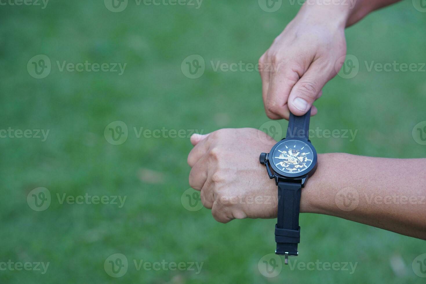 Close up man is wearing black leather hand watch, outdoor background. Concept, ashionable accessory for time telling, make you look stylish, punctual and smart. Analog wrist watch. photo