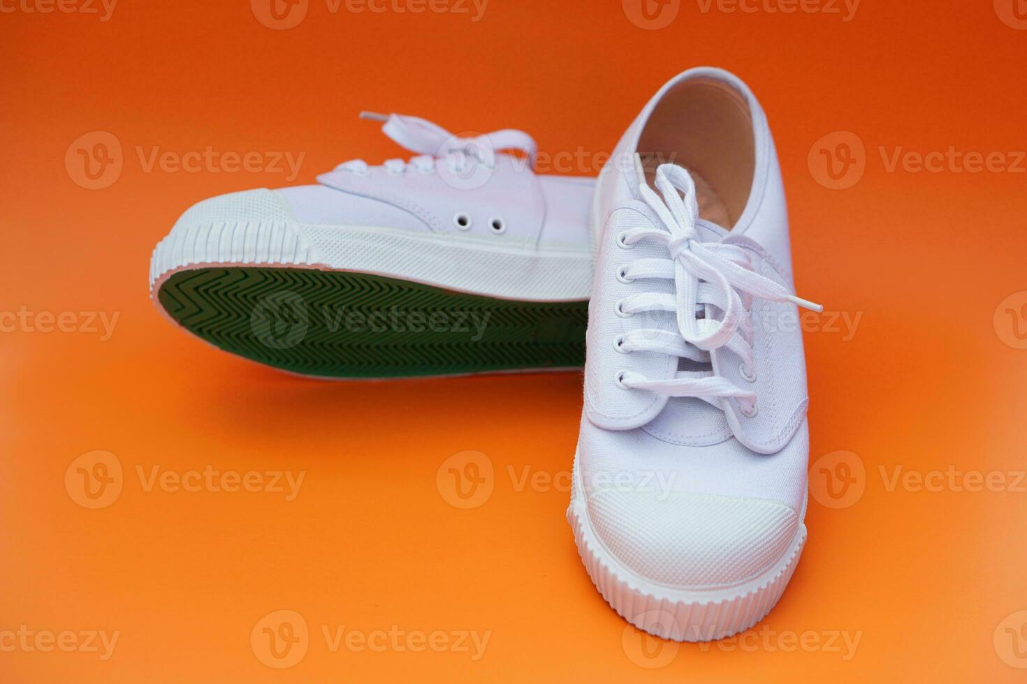 Pair of new white canvas sneakers, one shows green rubber under the shoes , orange background. Comfortable, fashionable. Concept, shoes for doing sport or exercise also can wear for traveling, hiking. photo