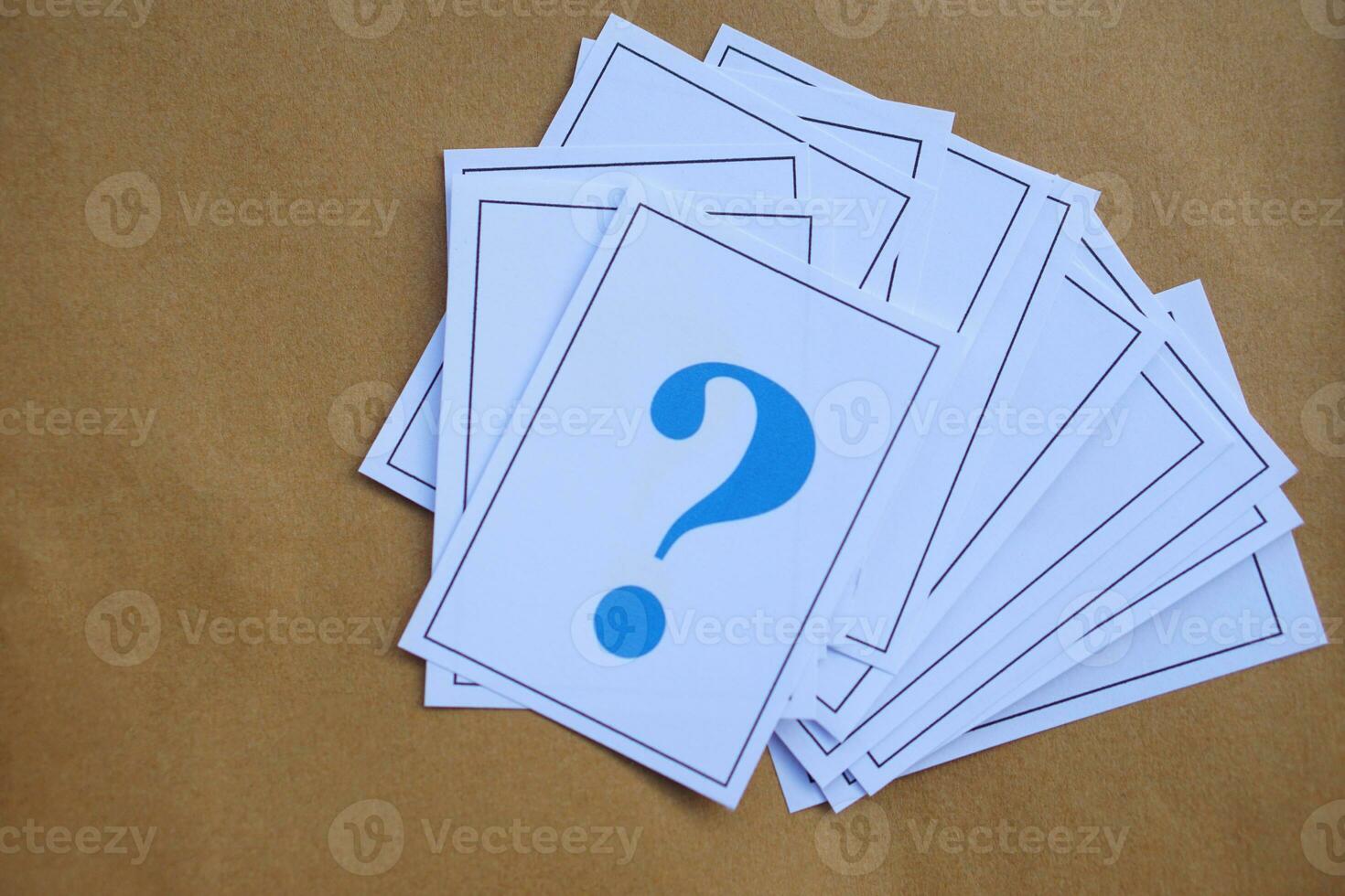 Pile of overlapped paper cards of blue  question marks, brown background. Concept. Teaching aid. Education materials for doing activity or playing games about find answers. photo