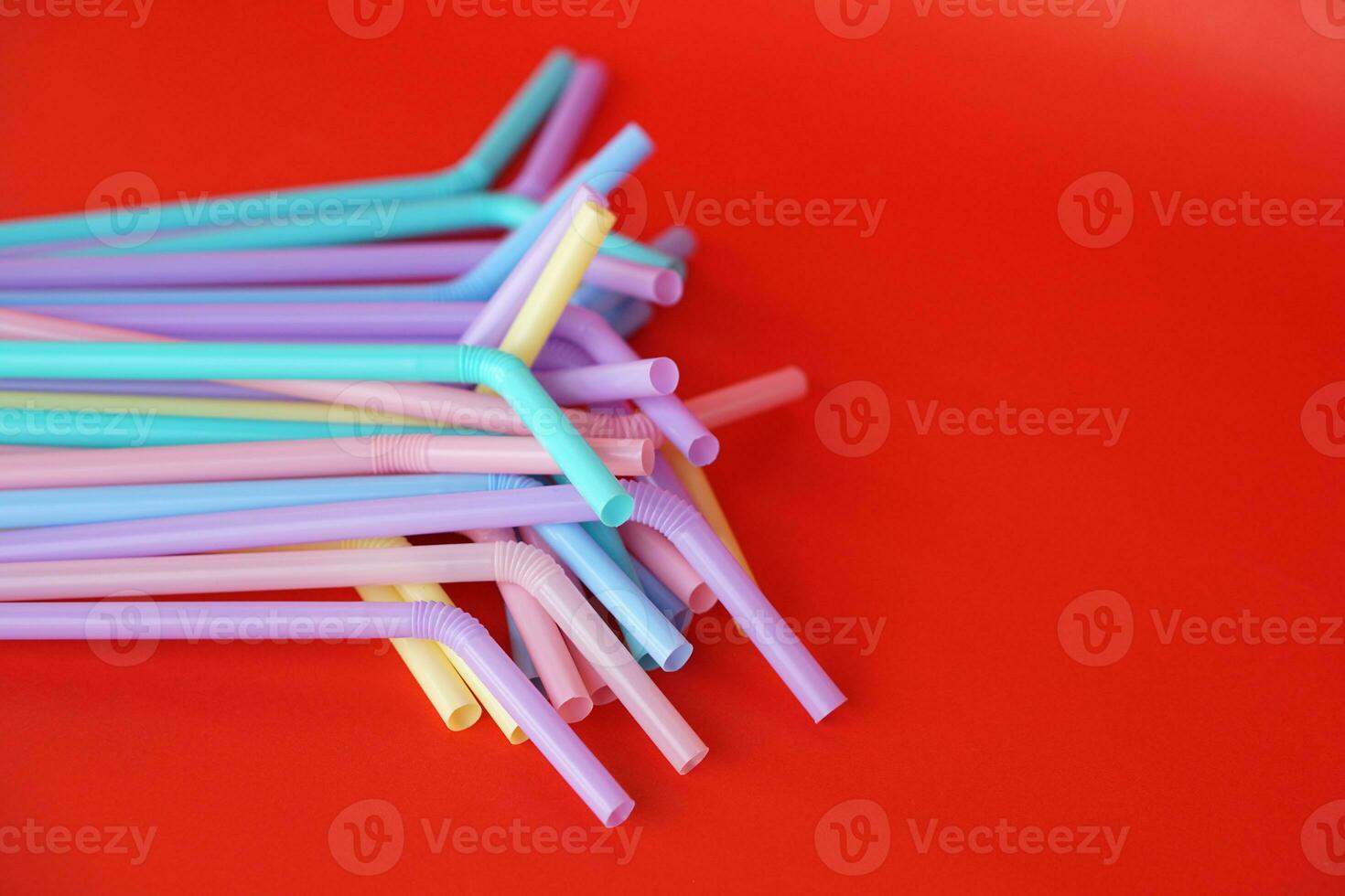 Colorful plastic drinking straws tubes for juice and cocktails, red background. Concept, single use equipment for drinking, but can use for diy crafts for decoration. photo