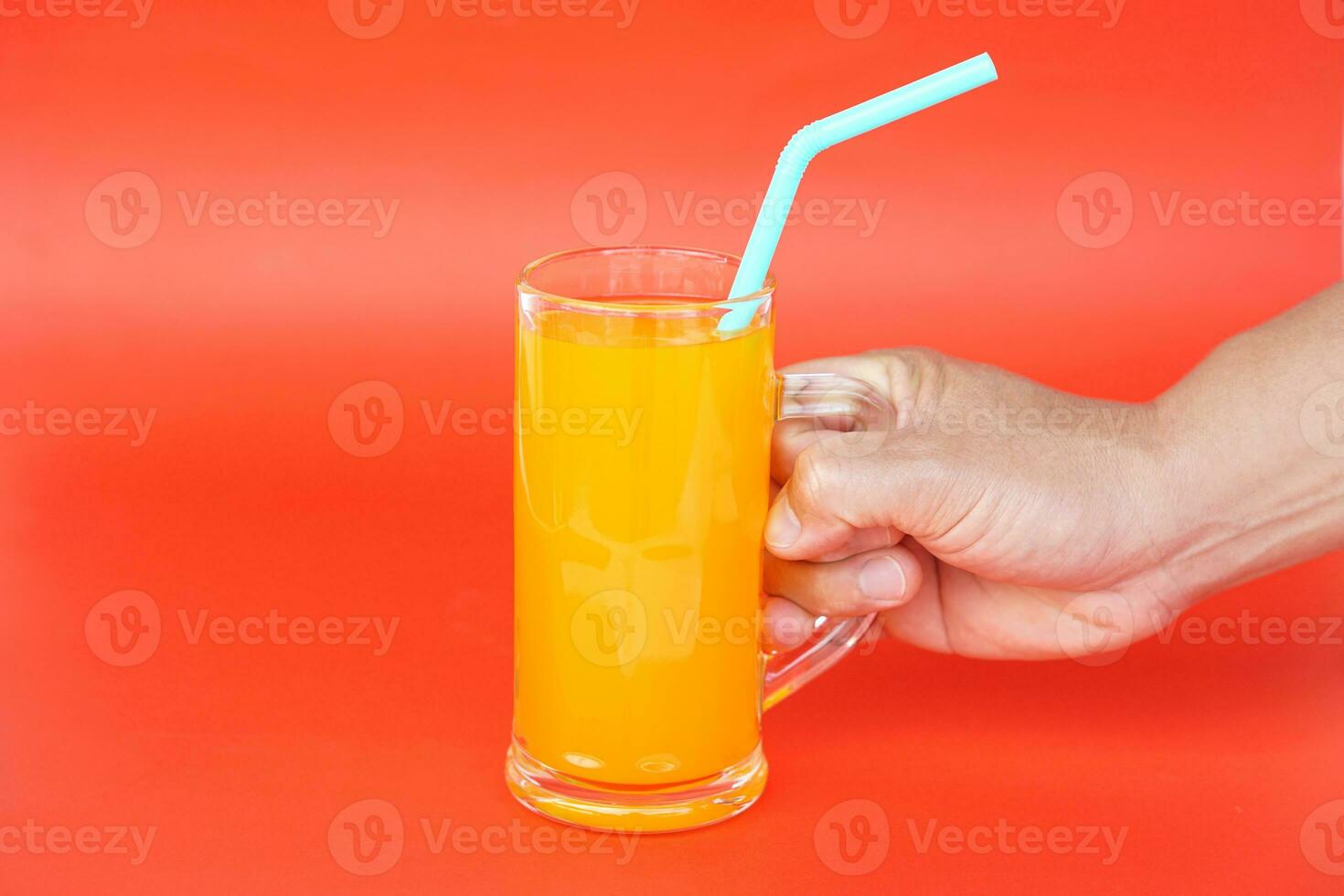 Close up of man hand holding glass of orange juice with drinking straw, on red background. Concept, morning refreshing beverage. Sweet, testy and high vitamin C. photo