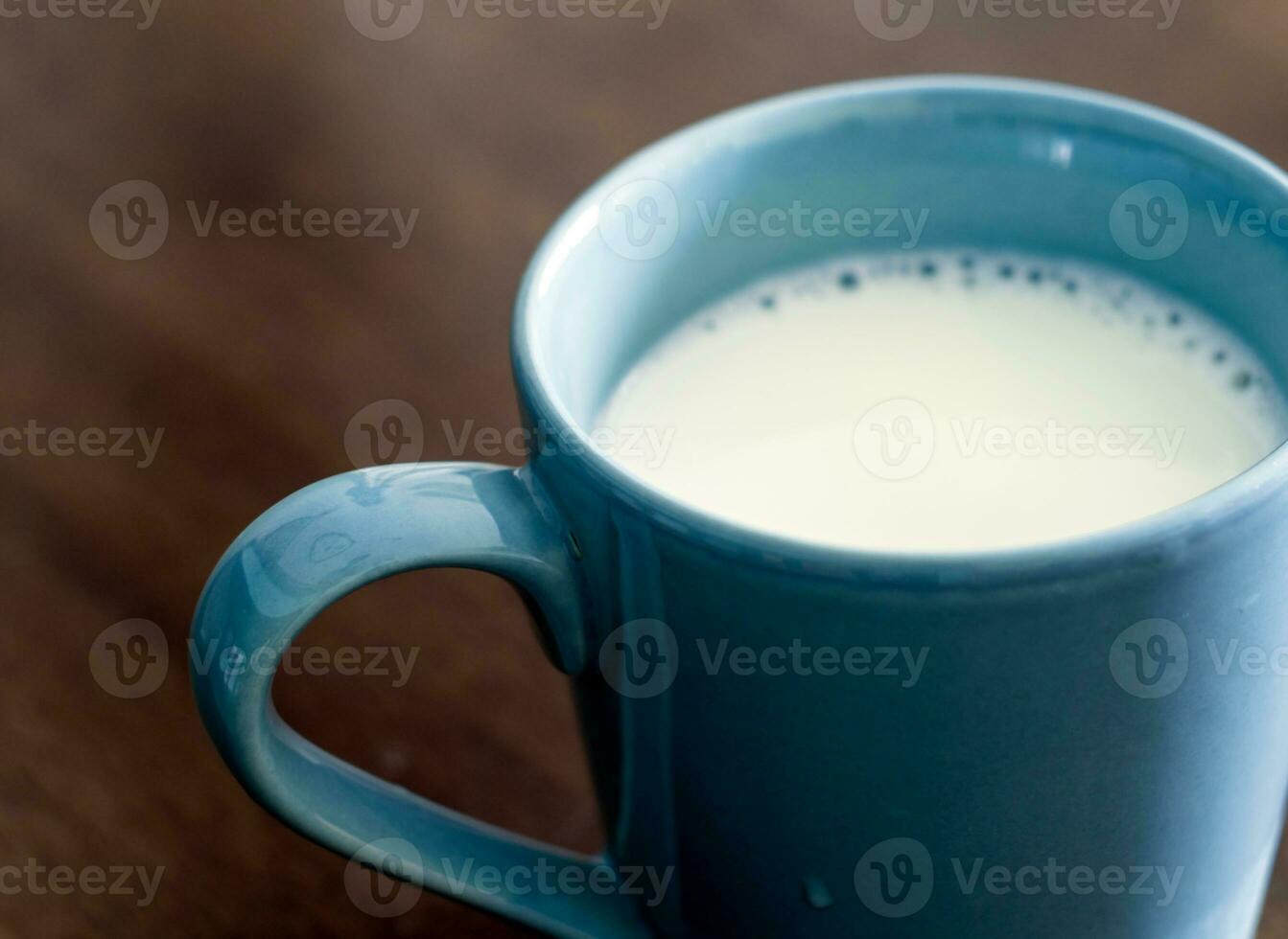 Milk in a blue cup on the wooden and top glass table photo