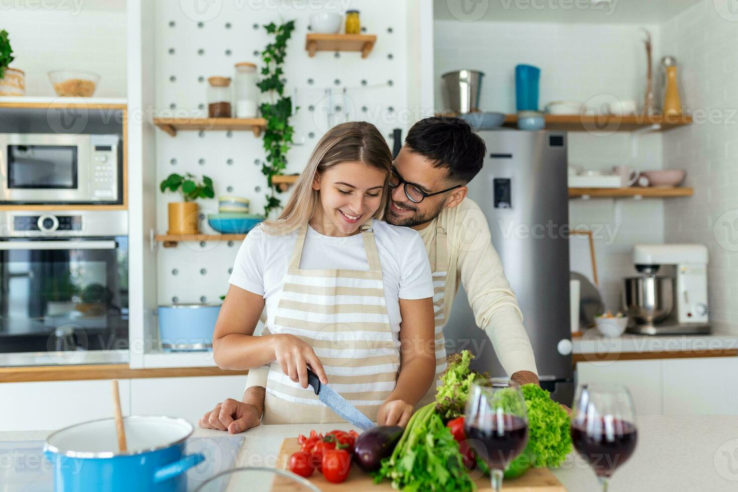 Affectionate young man kissing his wife while she's making breakfast. Beautiful young couple is talking and smiling while cooking healthy food in kitchen at home.Man is kissing his girlfriend in cheek photo