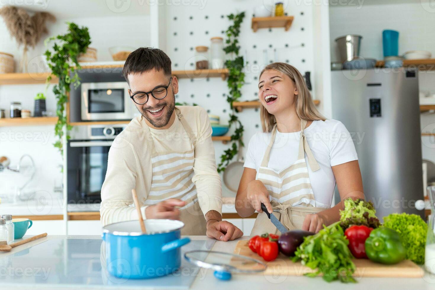 Beautiful young couple is feeding each other and smiling while cooking in kitchen at home. Happy sporty couple is preparing healthy food on light kitchen. Healthy food concept. photo