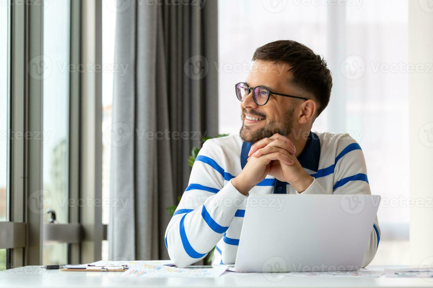 Smiling man in glasses sit at desk in office browsing wireless Internet on laptop device, happy male worker relax at work break photo