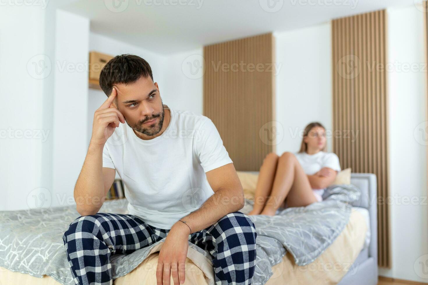Beautiful girl and a frustrated man sitting in bed and not looking at each other. Upset couple ignoring each other. Worried man in tension at bed. Young couple angry with each other after a fight. photo
