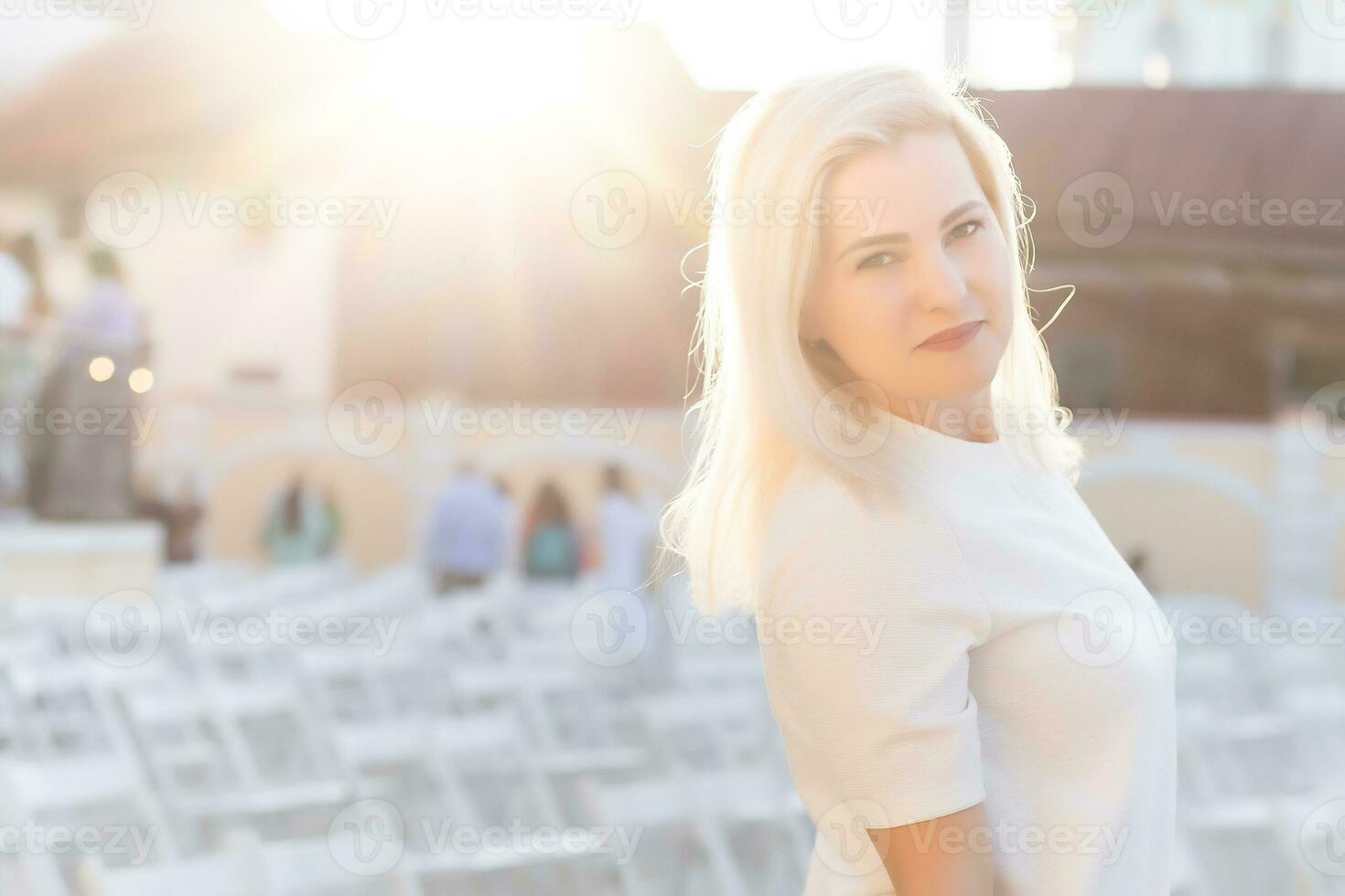 attractive woman dressed in white dress in summer open air theater on chair alone, spring street style fashion trend, social distancing photo