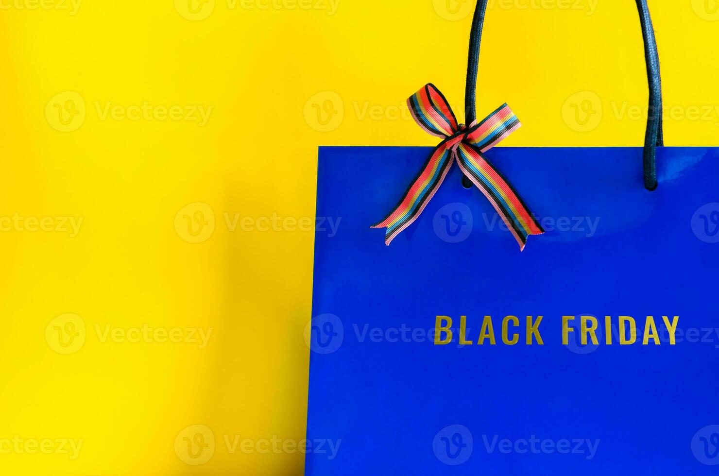 Blue shopping bag with ribbon and Black Friday word on yellow background for Black Friday shopping  concept. photo
