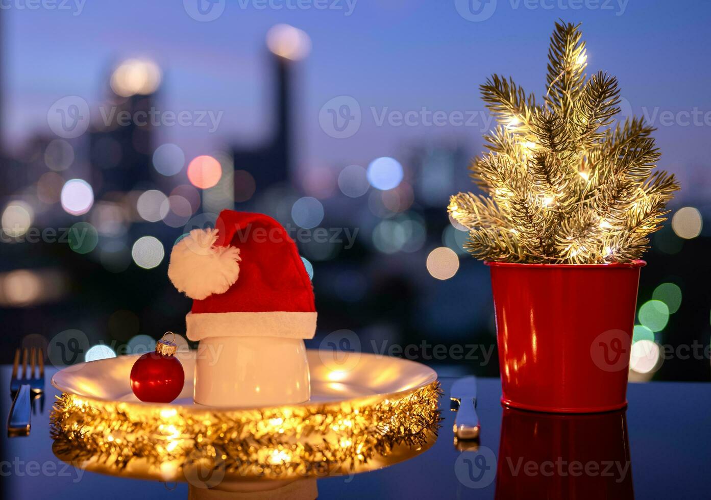 Christmas dining concept with white plate which have small bowl that have santa claus hat on it put on table with city bokeh light background. photo