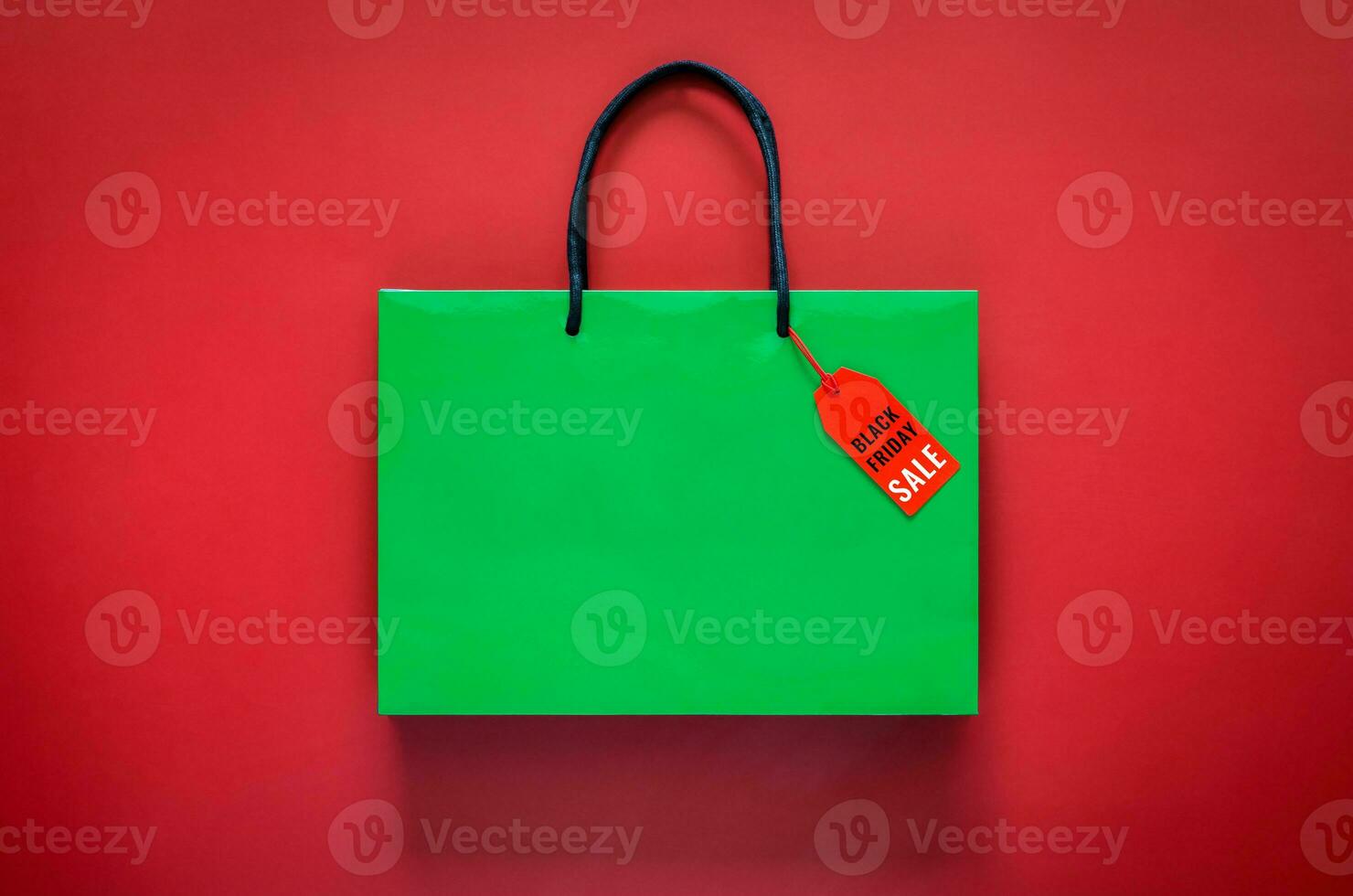 Green shopping paper bag with word at price tag on red background for Black Friday shopping sale concept. photo