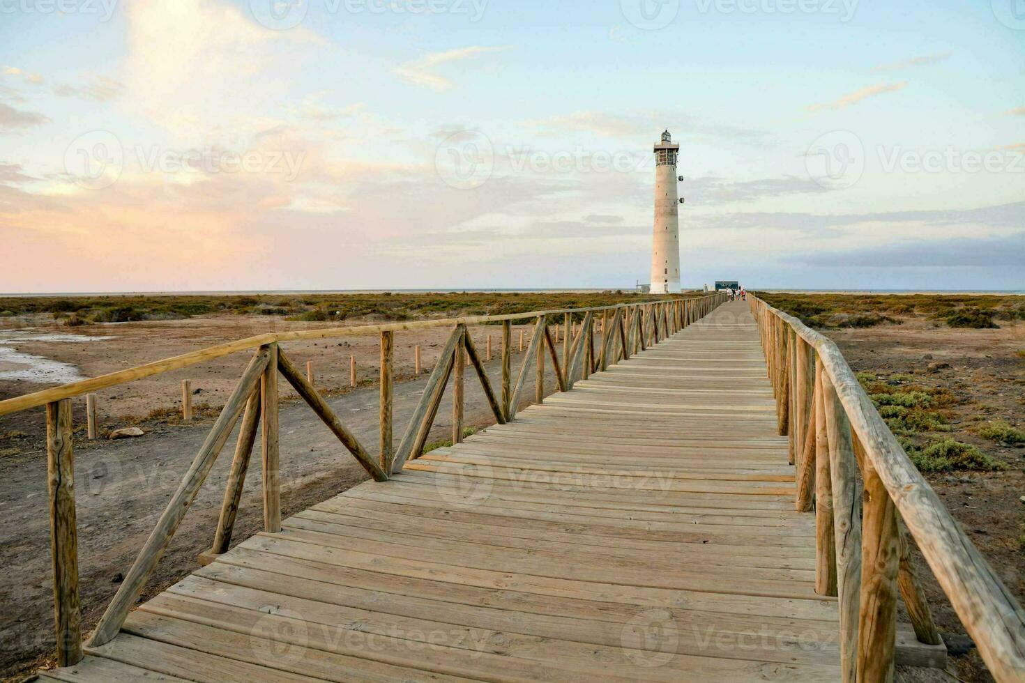 un de madera pasarela Guías a un faro a puesta de sol foto