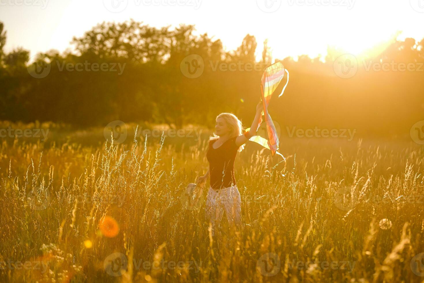 Beauty girl running with kite on the field. Beautiful young woman with flying colorful kite over clear blue sky. Free, freedom concept. Emotions, healthy lifestyle photo