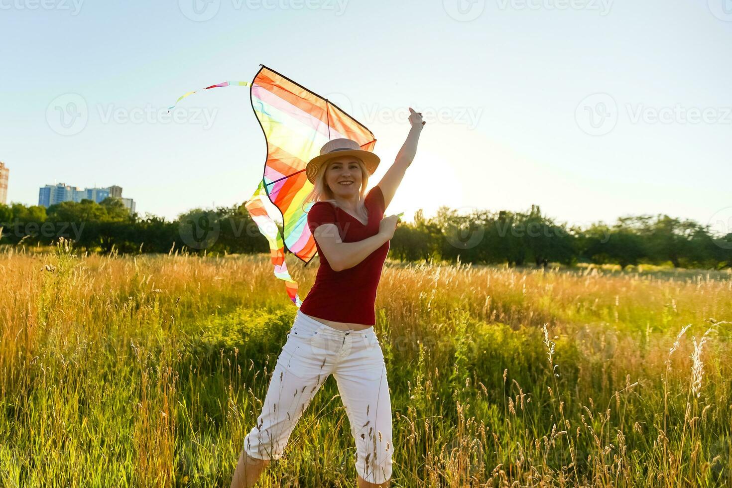 Beauty girl running with kite on the field. Beautiful young woman with flying colorful kite over clear blue sky. Free, freedom concept. Emotions, healthy lifestyle photo