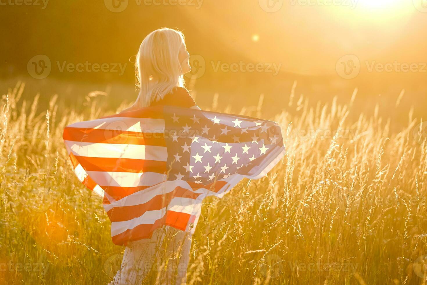 hermosa joven niña participación un americano bandera en el viento en un campo de centeno. verano paisaje en contra el azul cielo. horizontal orientación. foto