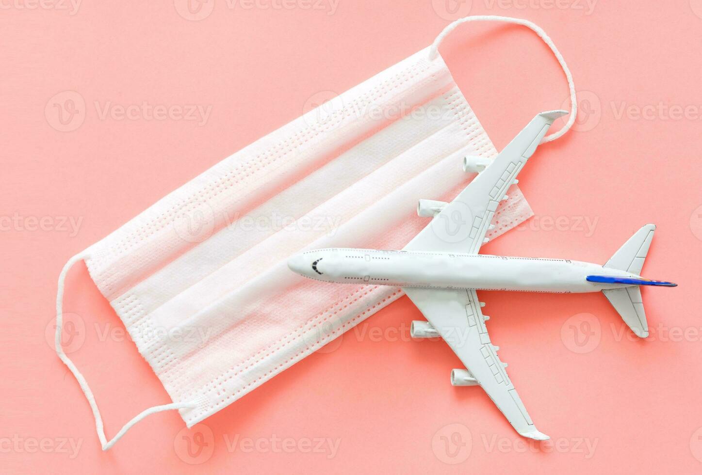 Plane model and face medical mask on a pink background . Flight cancellation due to the impact of coronavirus. photo