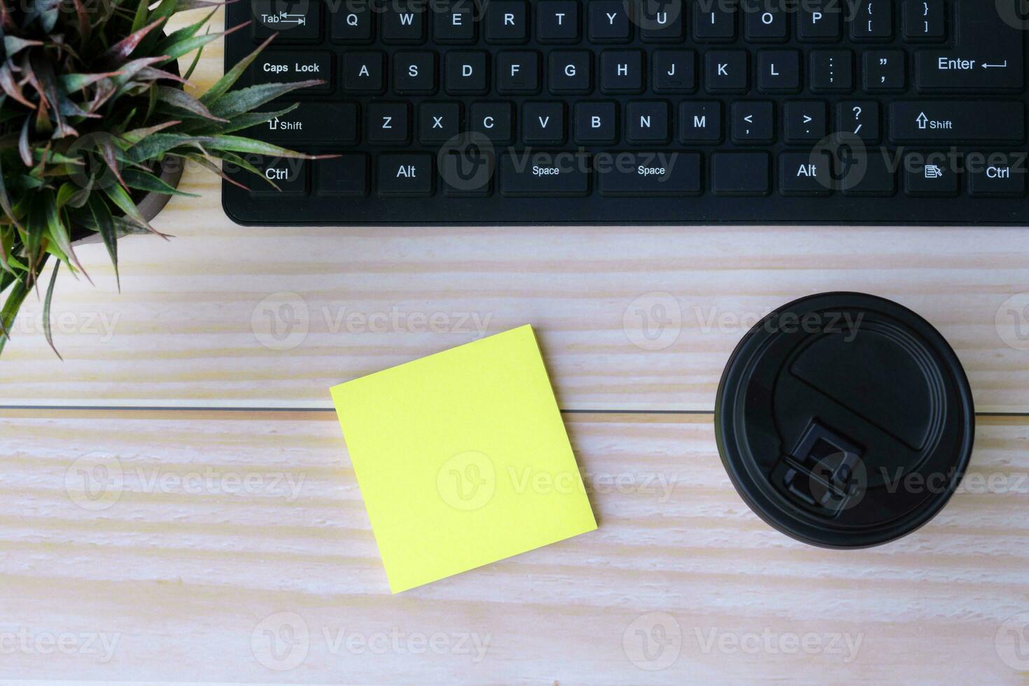 Sticky note with disposable coffee cup, computer keyboard and potted plant. photo