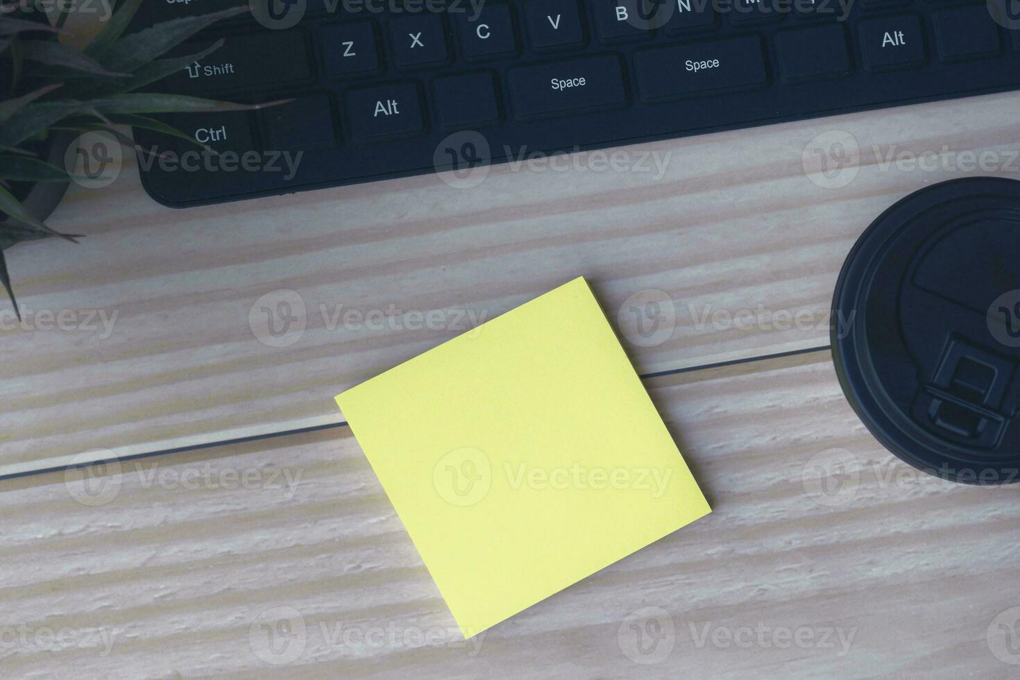 Sticky note with disposable coffee cup, computer keyboard and potted plant. photo