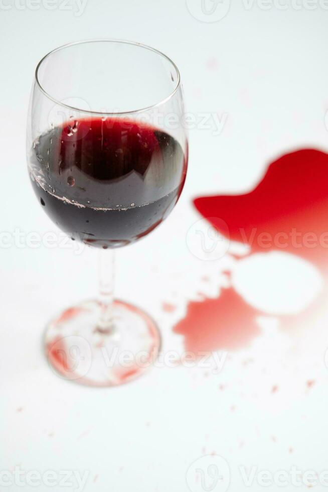 rojo vino en un transparente vaso y derramado bebida en un blanco antecedentes foto