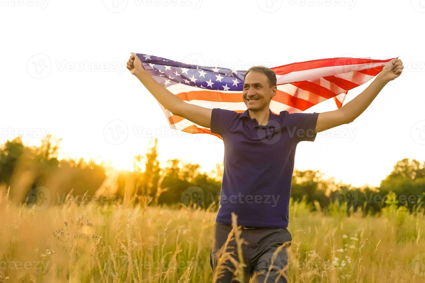 cuarto de julio. patriótico hombre con el nacional americano bandera en el campo. joven hombre con orgullo ondulación un americano bandera. independencia día. foto