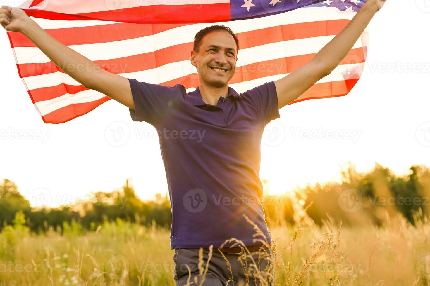 cuarto de julio. patriótico hombre con el nacional americano bandera en el campo. joven hombre con orgullo ondulación un americano bandera. independencia día. foto