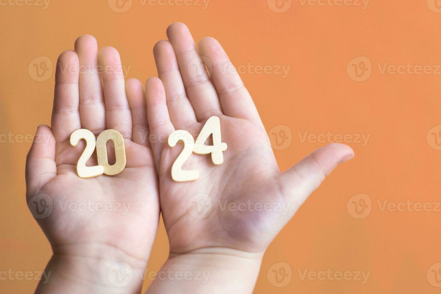Child hands holding wooden number 2024 on palms on festive Peach Fuzz background with copy space photo