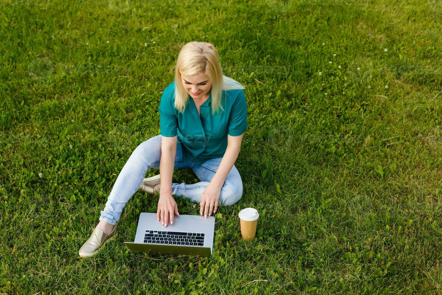 Top view of woman sitting in park on the green grass with laptop, hands on keyboard. Computer screen mockup. Student studying outdoors. Copy space for text photo