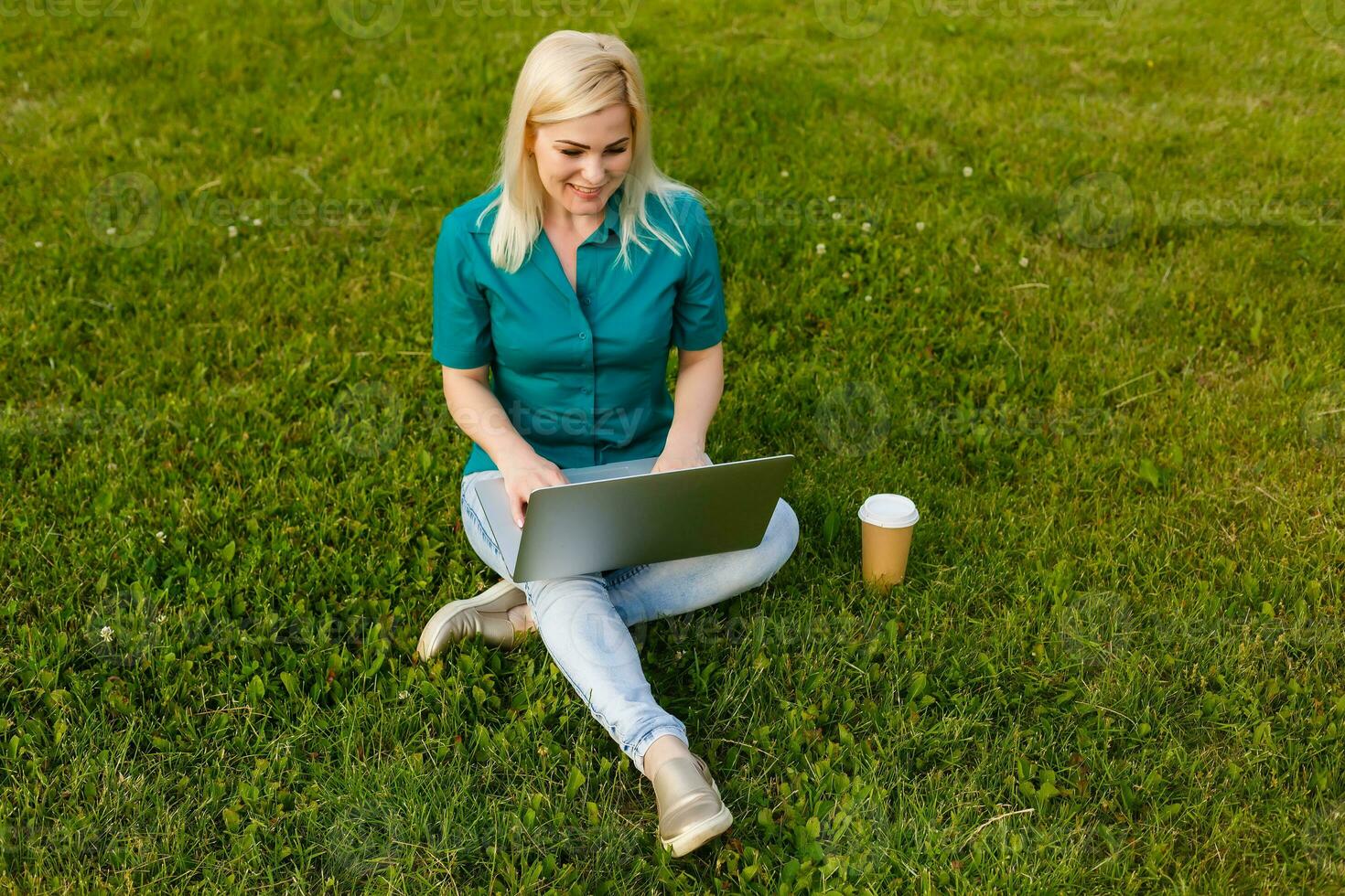 Top view of woman sitting in park on the green grass with laptop, hands on keyboard. Computer screen mockup. Student studying outdoors. Copy space for text photo