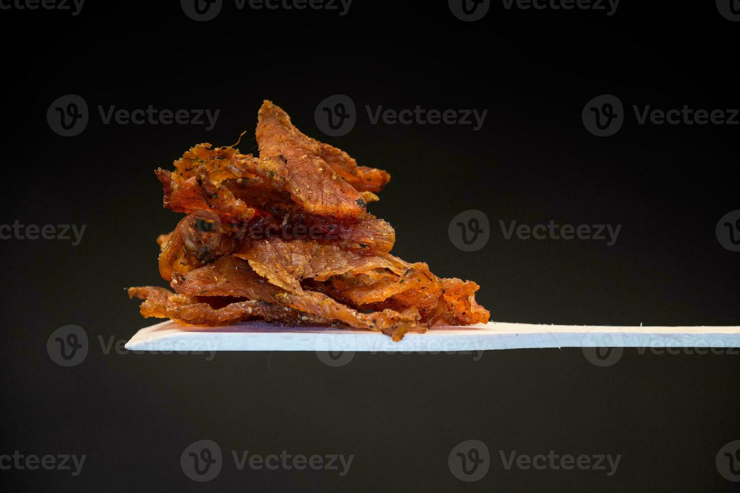 a handful of dried meat marinated with spices on a wooden spoon, isolated on a black background. photo