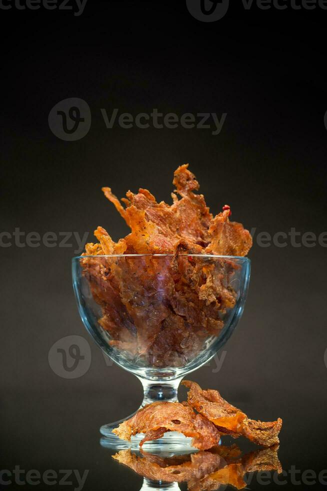 dried meat with spices in a glass bowl, isolated on black background photo