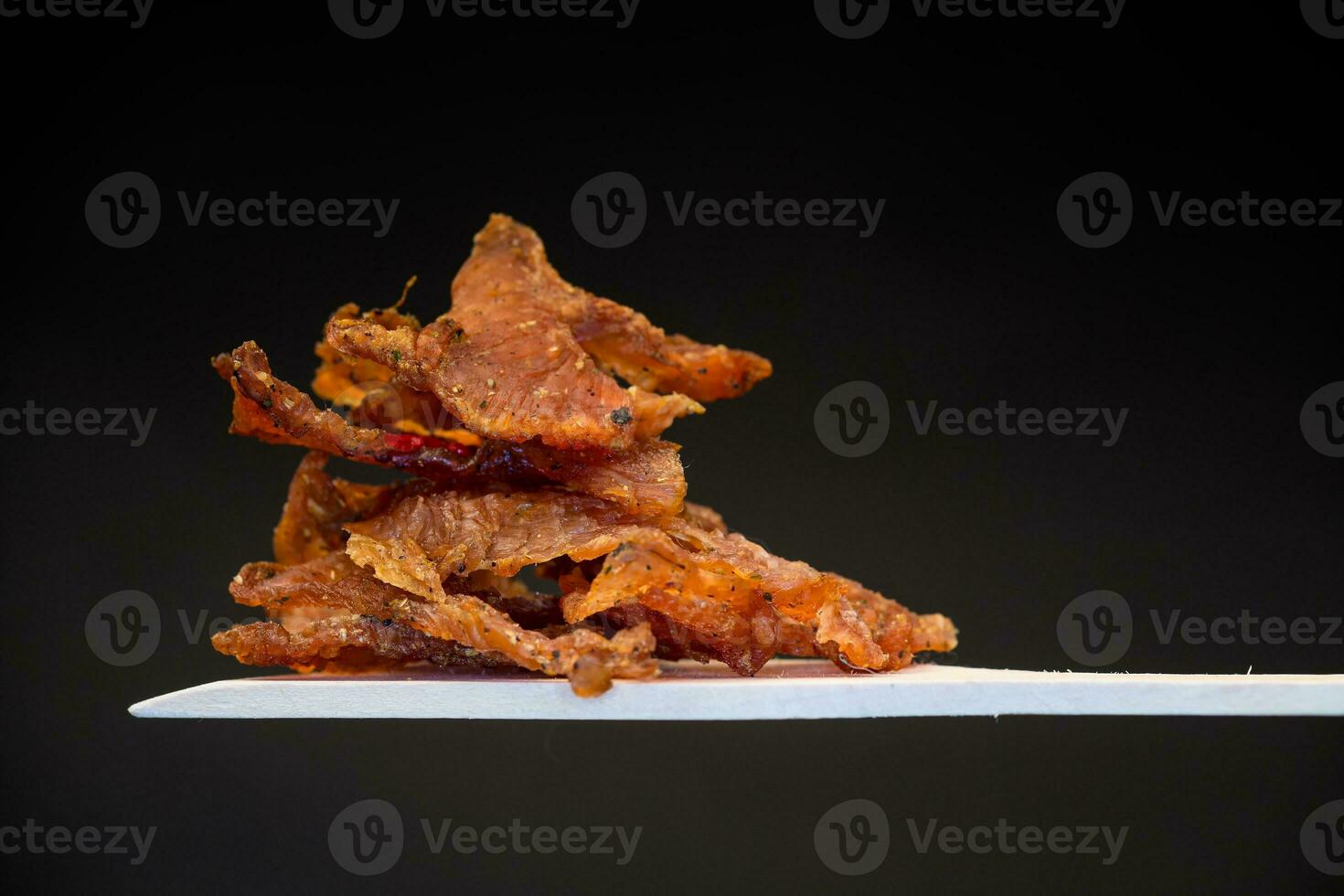 a handful of dried meat marinated with spices on a wooden spoon, isolated on a black background. photo