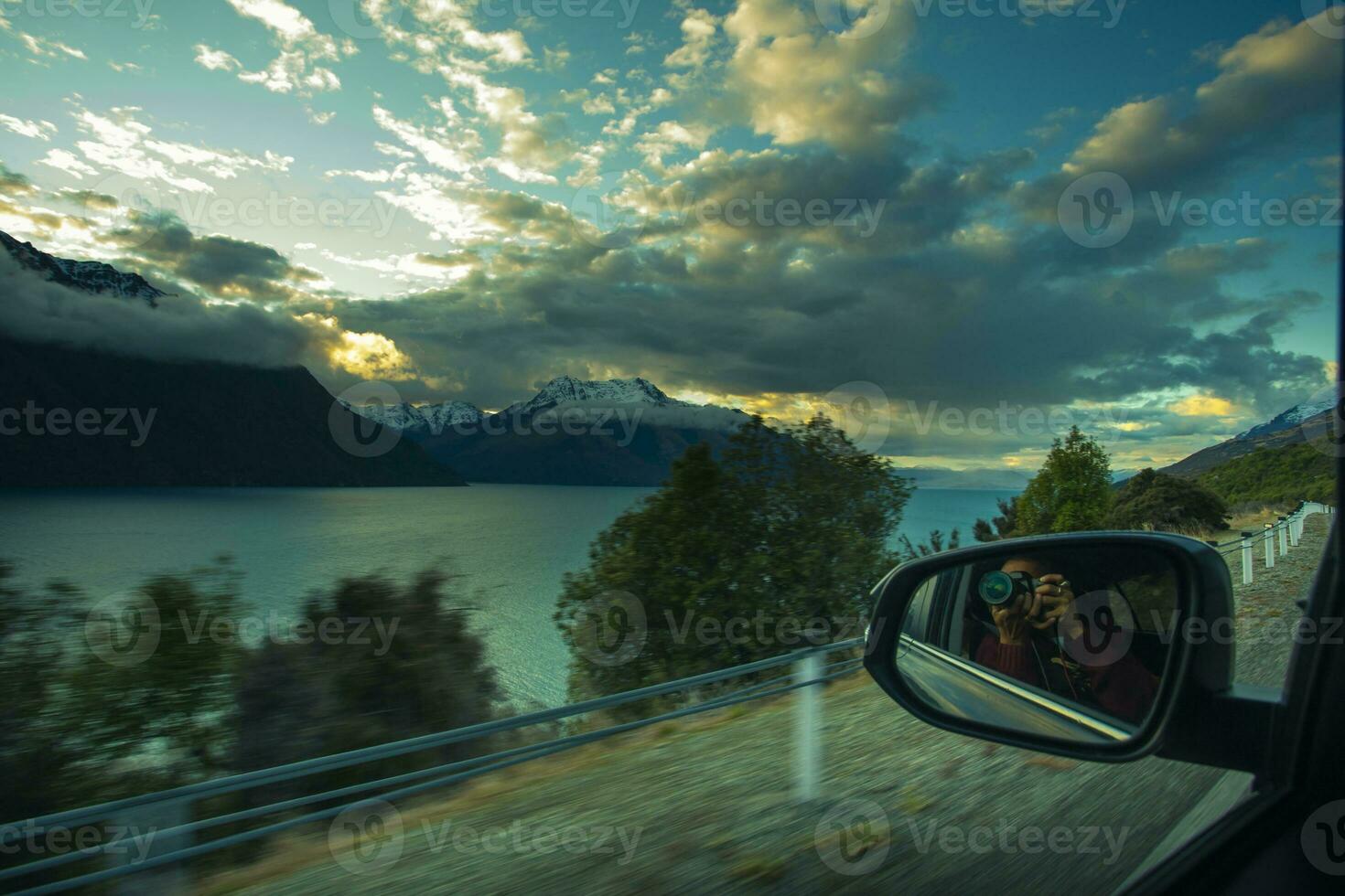 traveller taking a photo of lake wakatipu while car driving on queentown road
