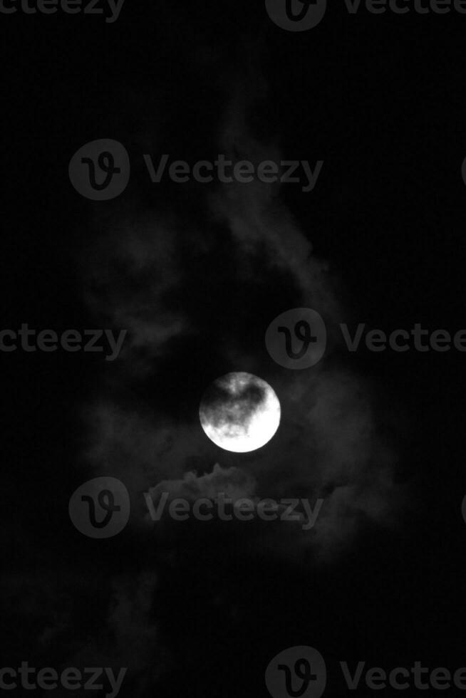 Full moon light behind clouds in black and white photo