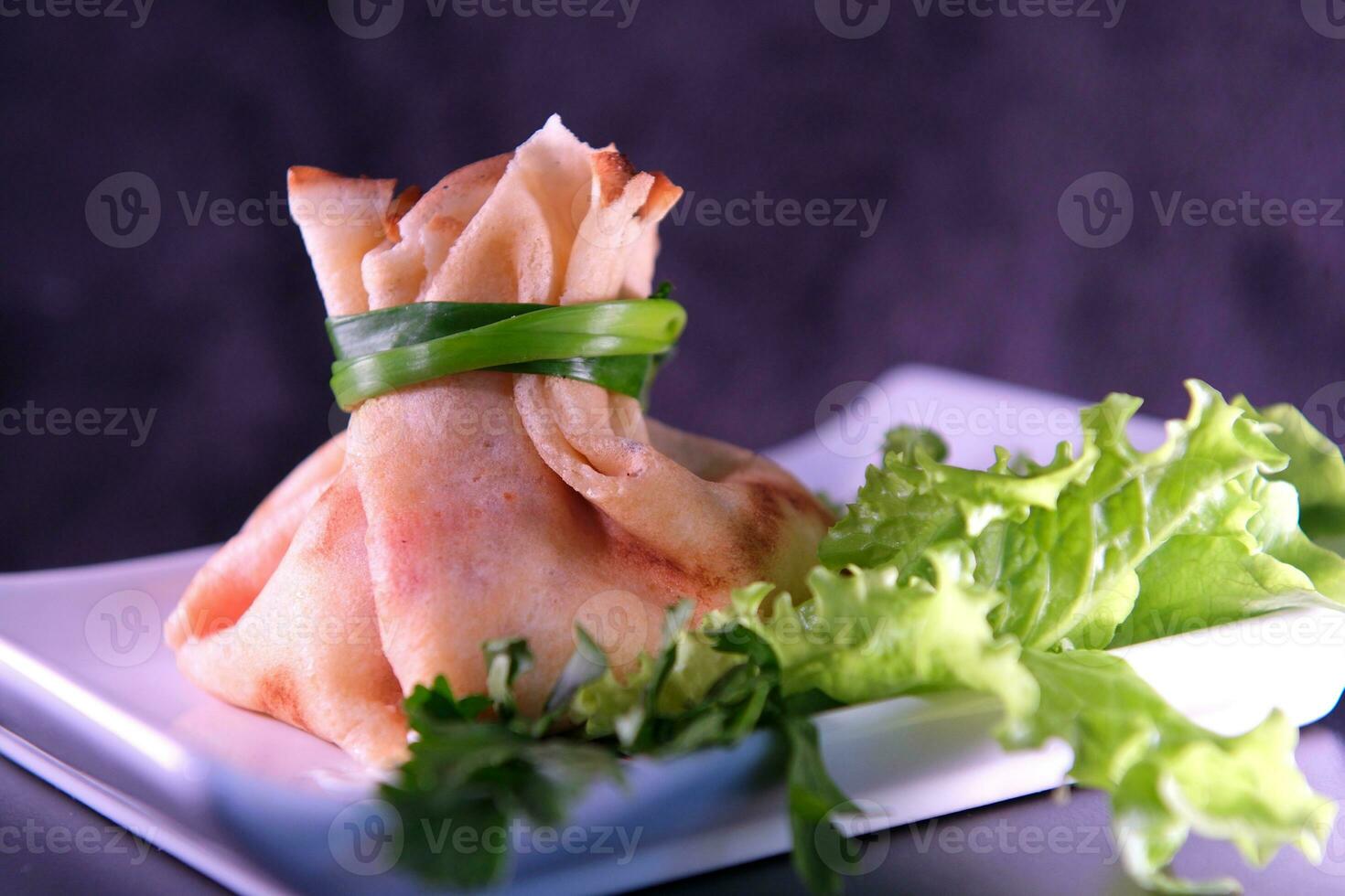 tortita con rojo caviar y mayonesa hecho en un bolso atado con verde cebollas en un blanco cuadrado plato perejil lechuga hojas ucranio eslavo comida foto