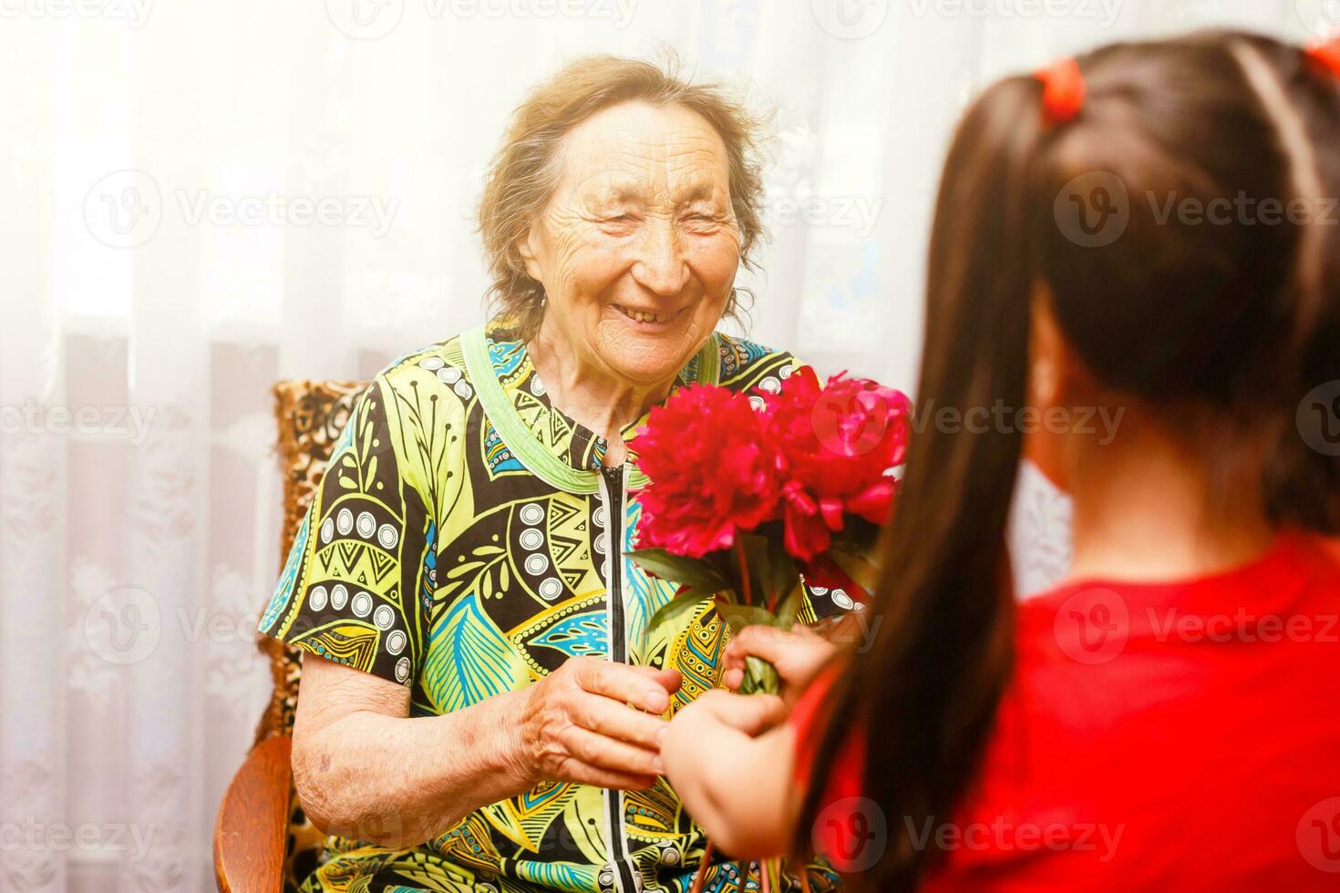 little girl giving her great grandmother a pink flower photo