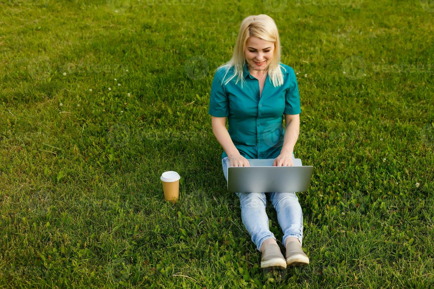 Top view of woman sitting in park on the green grass with laptop, hands on keyboard. Computer screen mockup. Student studying outdoors. Copy space for text photo