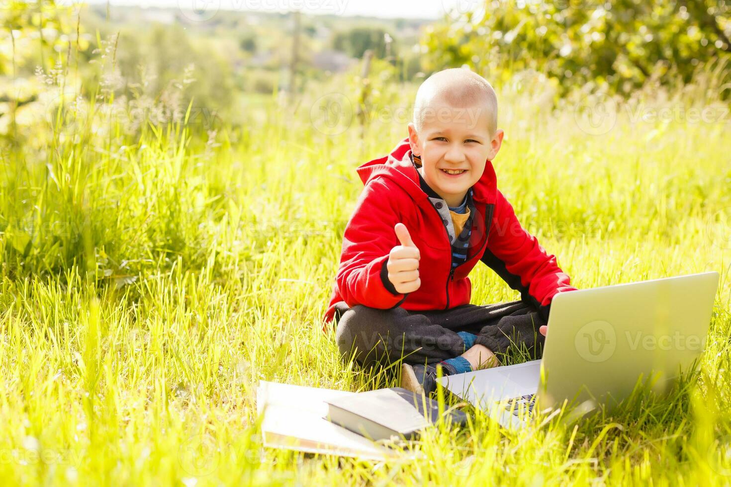 young boy with a books and laptop computer on green grass in the park photo