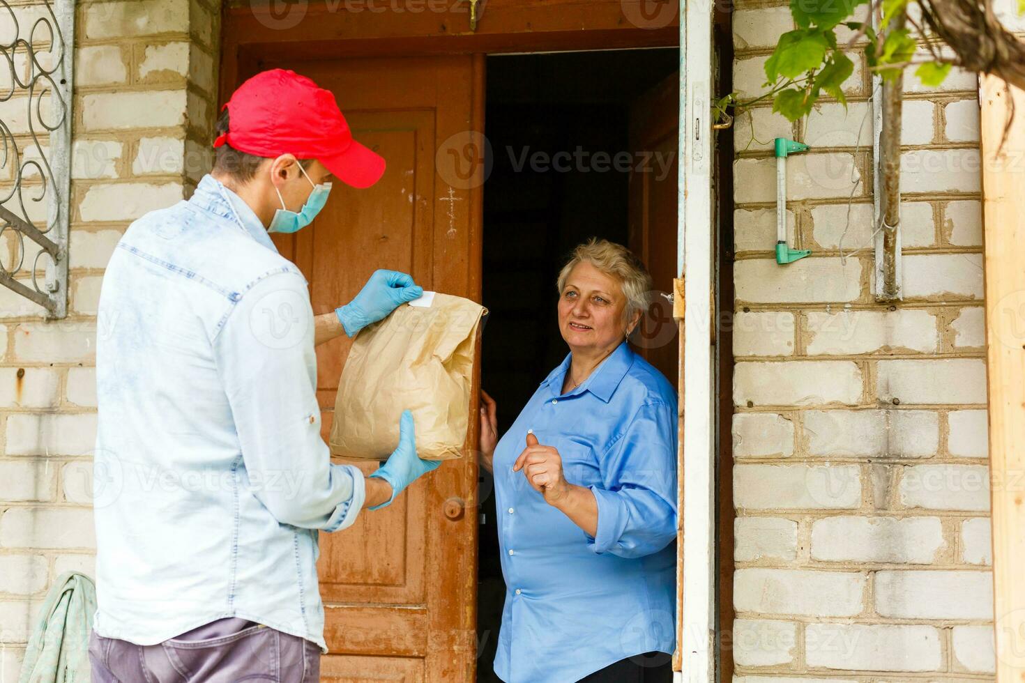 un mayor mujer corsé a hogar. comida entrega en un médico mascarilla. foto